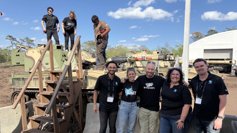A group of Huntress employees pose in front of tanks.