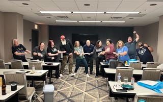Applied Systems employees in a conference room pretend to play tug of war in a line