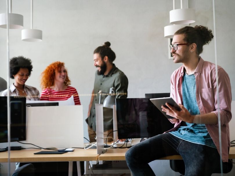 Three software engineers chat about an ongoing project while a fellow engineer brainstorms ideas while holding a tablet