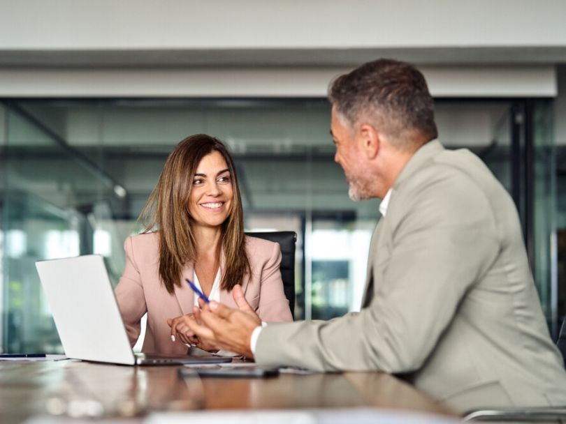 Two colleagues dressed in suits discuss an ongoing project in an office