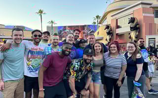 A group of Huntress employees pose outside for a photo in front of palm trees.