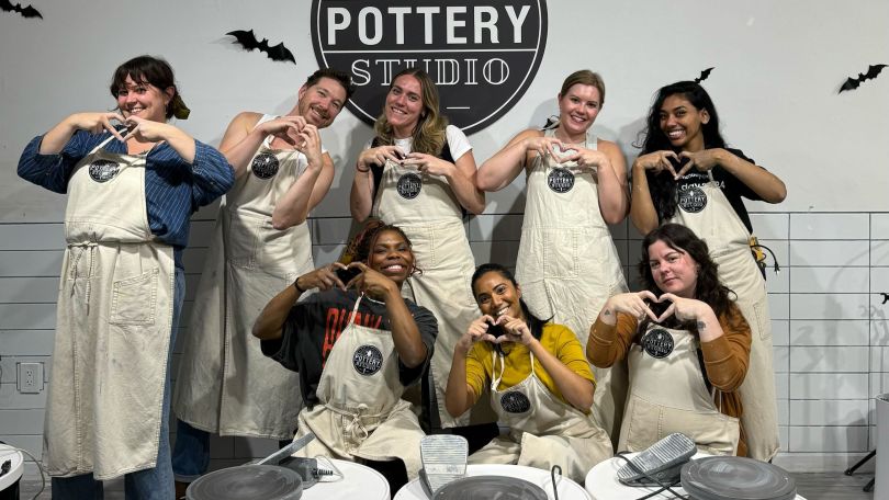 A group of monday.com employees pose in a pottery wheel studio for a group photo with their projects