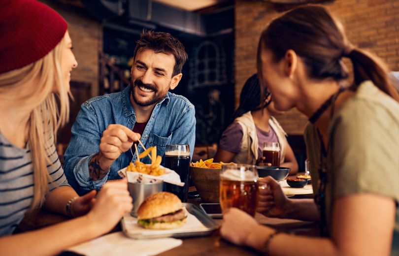 People smiling and eating french fries with toothpicks.