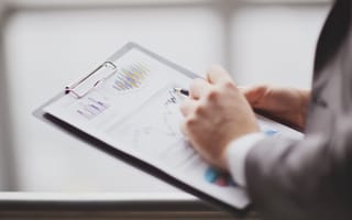 A person in a suit reviews graphs and charts on a clipboard, indicating analysis or business planning.
