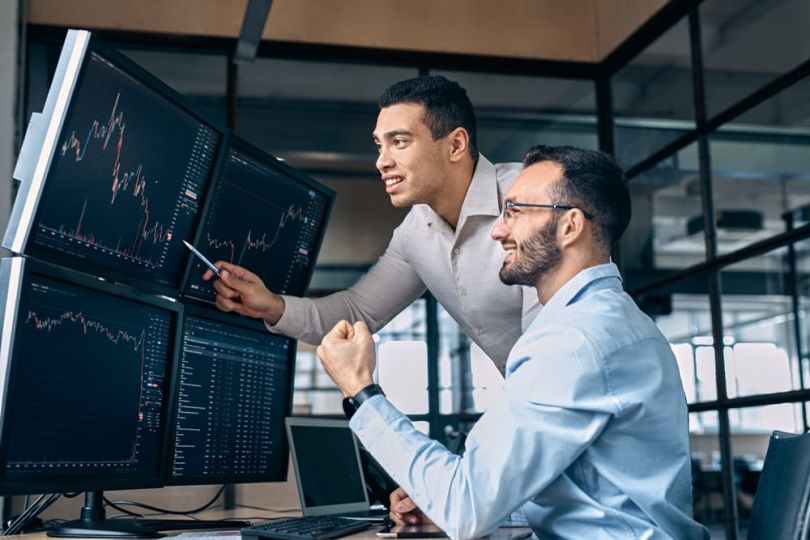 Two professionals looks at trading stats on a screen.